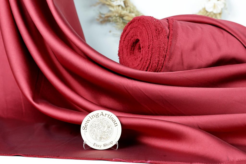 a red satin fabric with a rolled-up red fabric on top of it, placed on a white surface. There is also a small white plaque with text in front of the fabric.