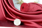 a red satin fabric with a rolled-up red fabric on top of it, placed on a white surface. There is also a small white plaque with text in front of the fabric.