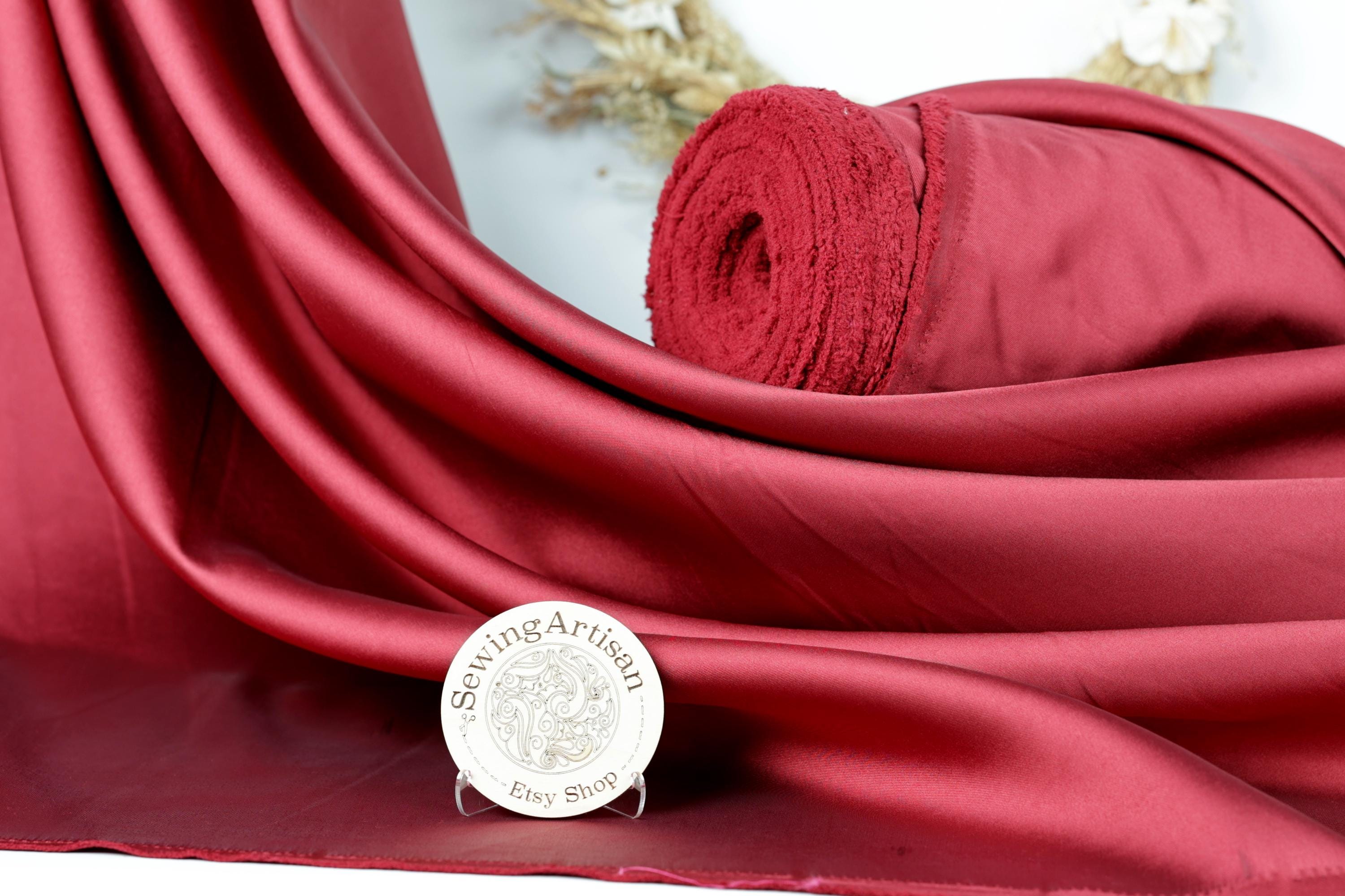 a red satin fabric with a rolled-up red fabric on top of it, placed on a white surface. There is also a small white plaque with text in front of the fabric.