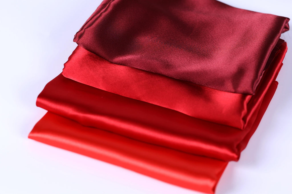 A stack of red and maroon satin fabric pieces, with the red fabric appearing more vibrant and the maroon fabric appearing more subdued.
