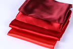 A stack of red and maroon satin fabric pieces, with the red fabric appearing more vibrant and the maroon fabric appearing more subdued.