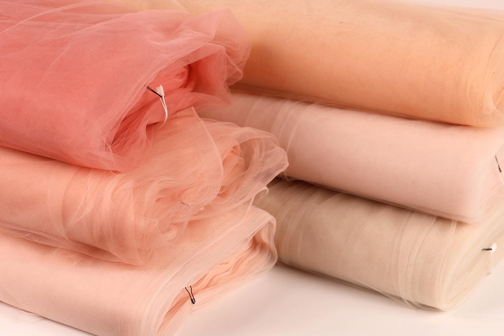 a collection of different colored tulle fabric, including pink, peach, and beige, neatly stacked on top of each other.