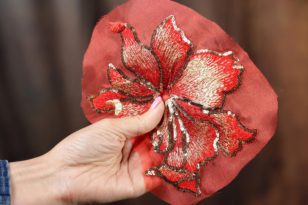 A hand holding a red fabric with a large, intricately embroidered flower design.
