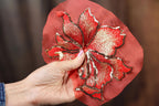 A hand holding a red fabric with a large, intricately embroidered flower design.