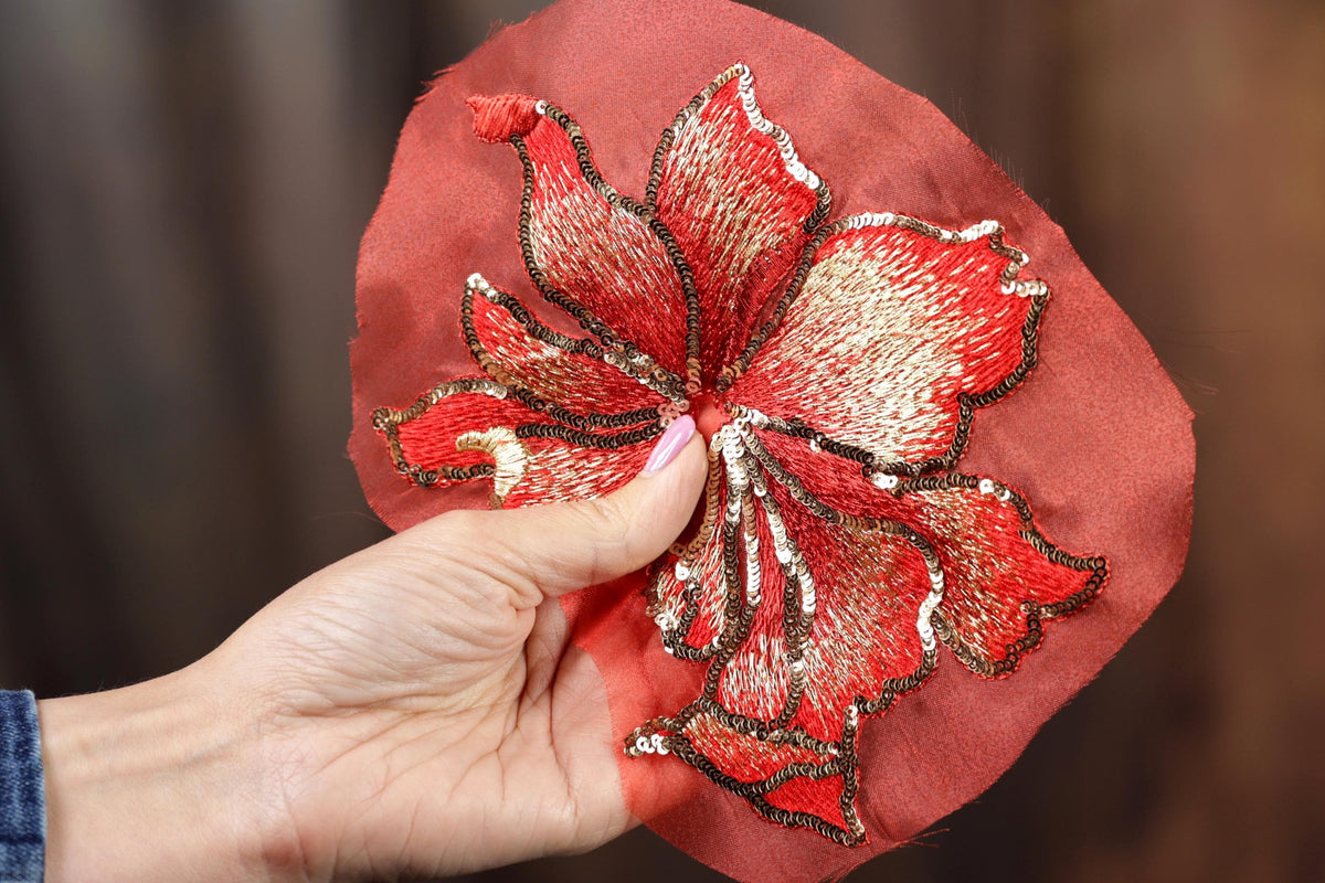 A hand holding a red fabric with a large, intricately embroidered flower design.