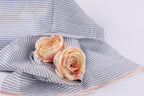 Two pink roses resting on a blue and white striped fabric.
