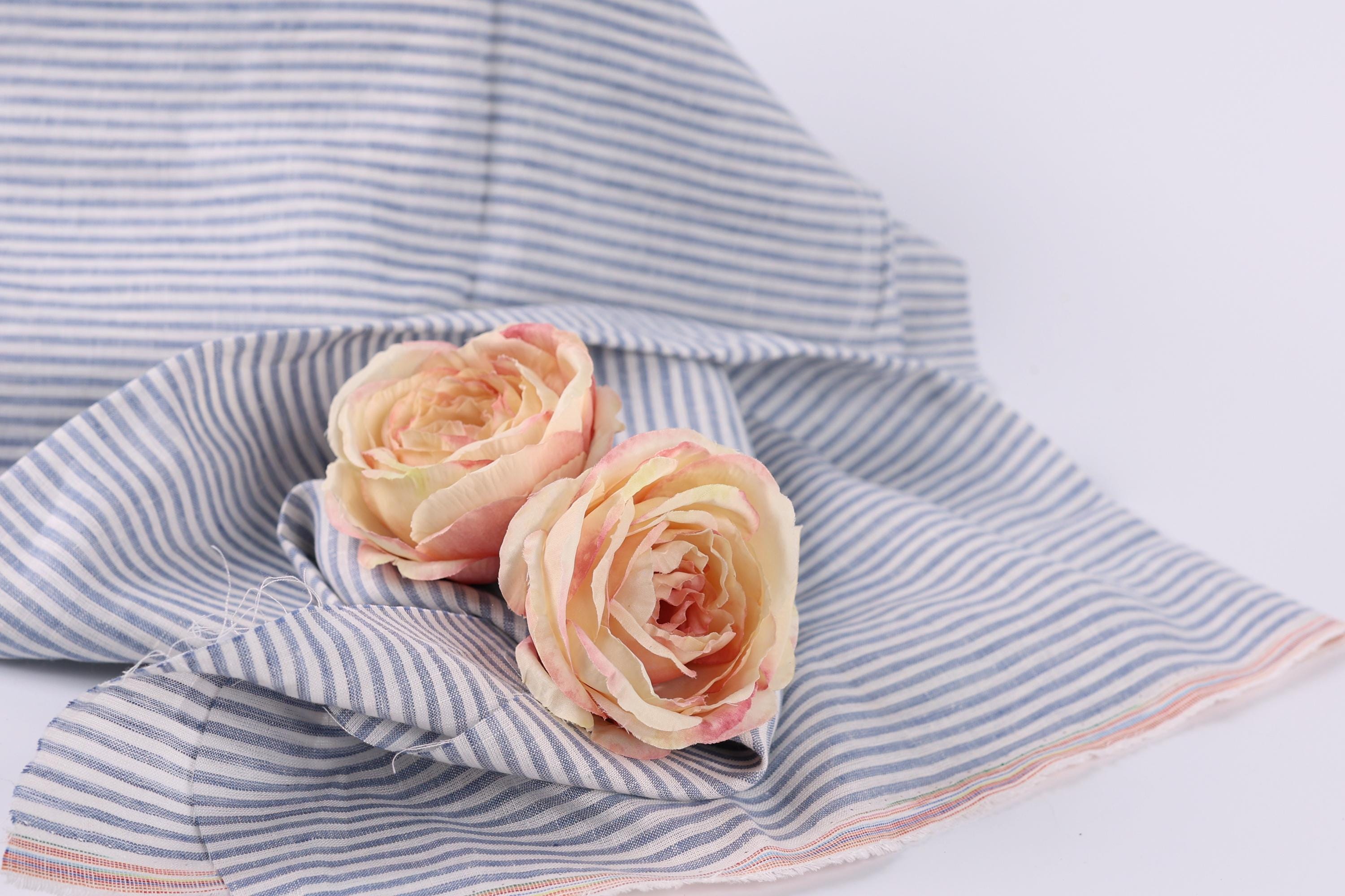 Two pink roses resting on a blue and white striped fabric.