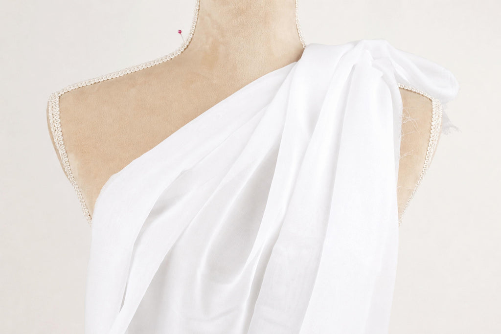A mannequin wearing a white draped dress with a beige bust and shoulders.