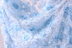 a close-up view of a delicate, light blue fabric with a floral pattern. The fabric appears to be made of a sheer material, with small white flowers or sequins scattered throughout the design. The overall appearance of the fabric is soft and delicate, with a sense of elegance and sophistication.