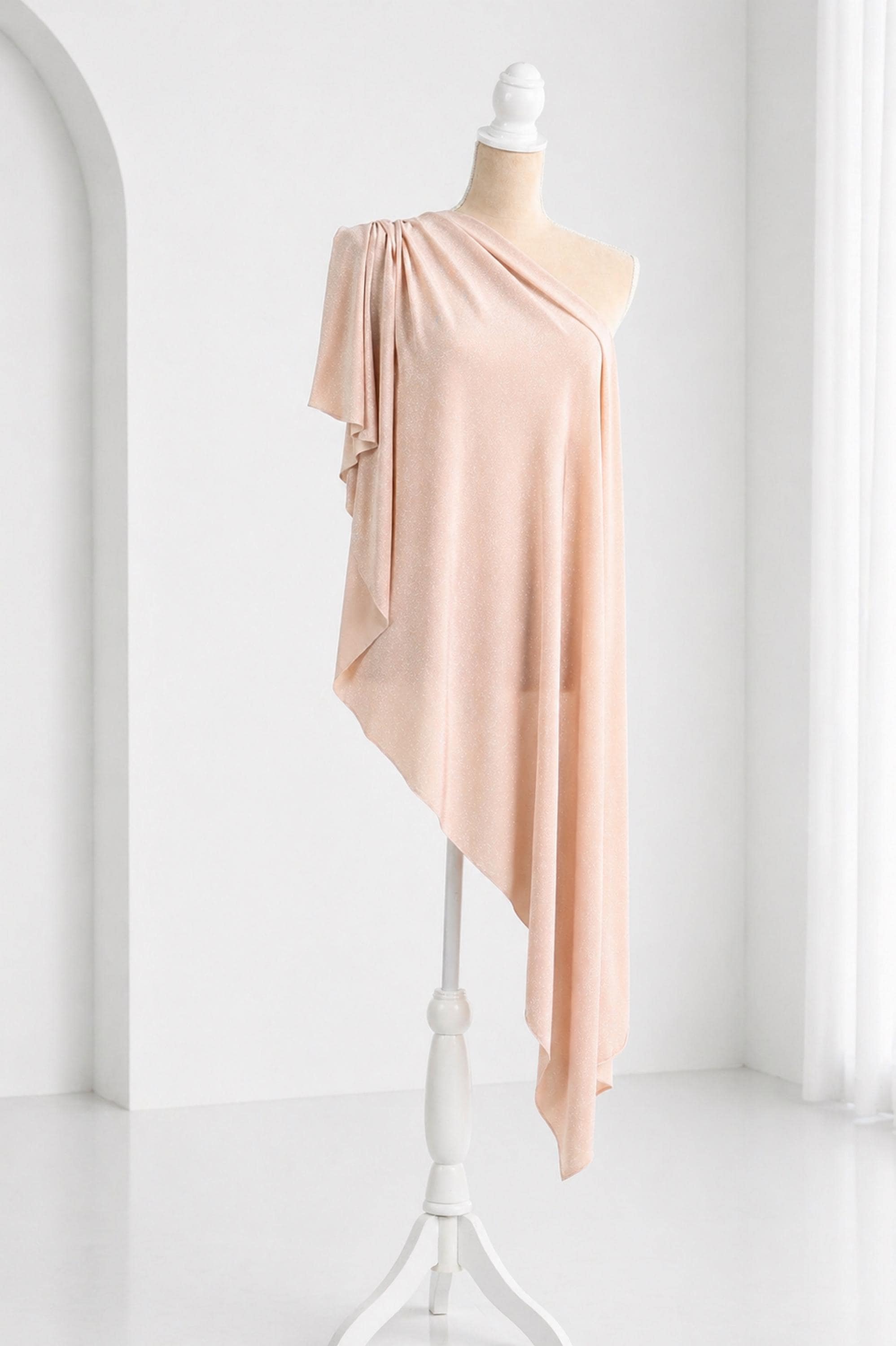 A mannequin wearing a peach-colored one-shoulder dress with a draped, flowing silhouette.