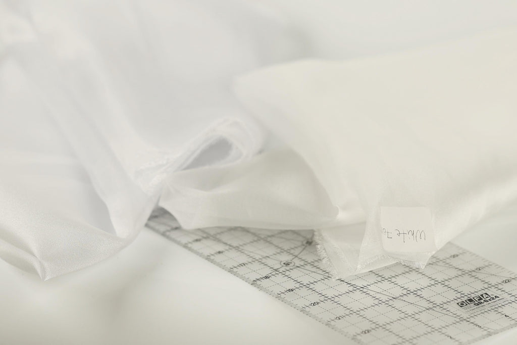 a close-up view of a white fabric, possibly a sheer or sheer-like material, with a ruler or measuring tape placed on top of it.