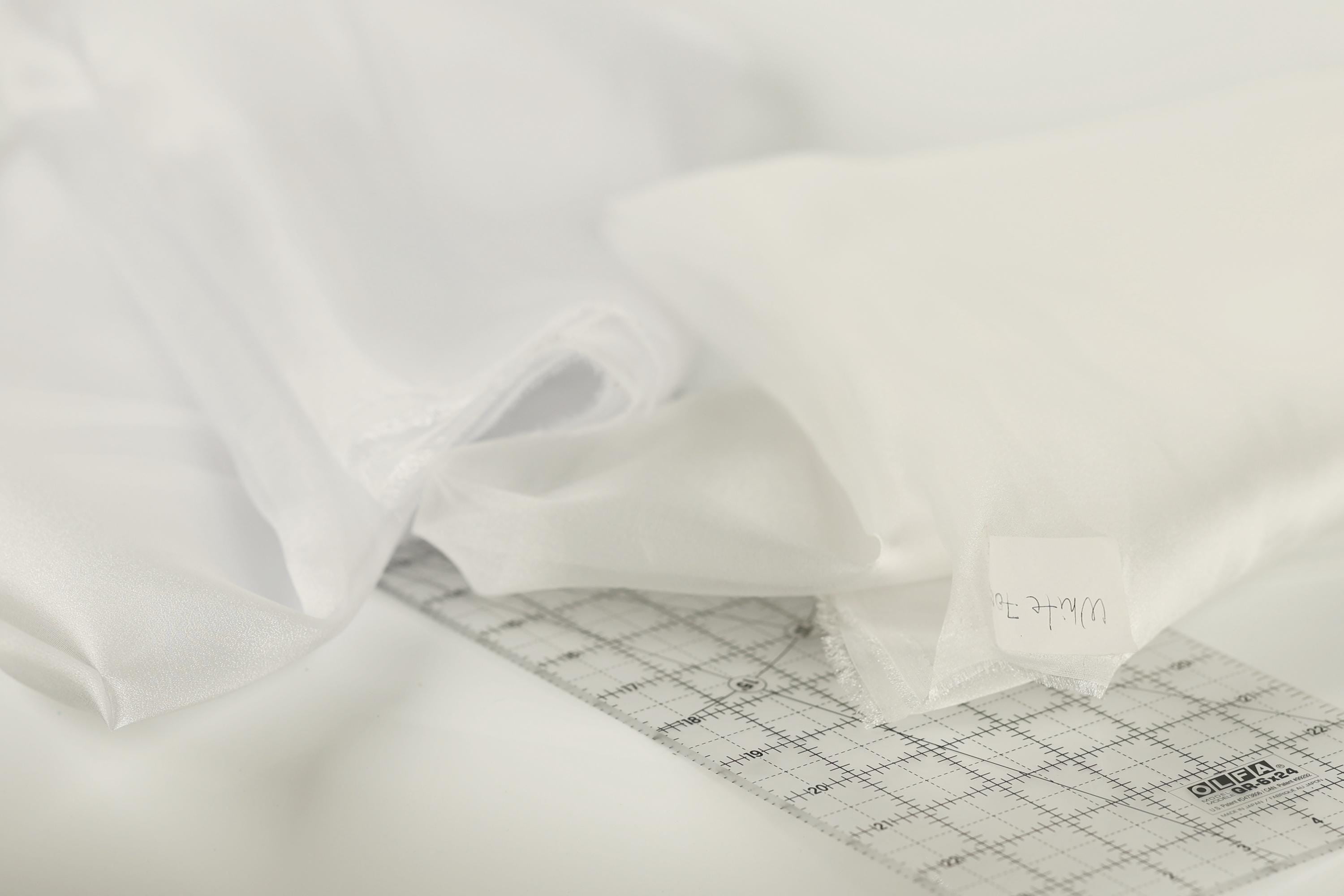 a close-up view of a white fabric, possibly a sheer or sheer-like material, with a ruler or measuring tape placed on top of it.