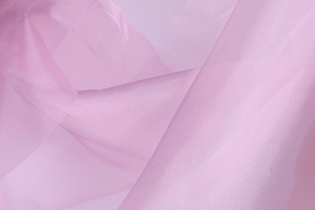The image is a close-up of a soft, light pink fabric, possibly silk or chiffon, with a slightly wrinkled texture.