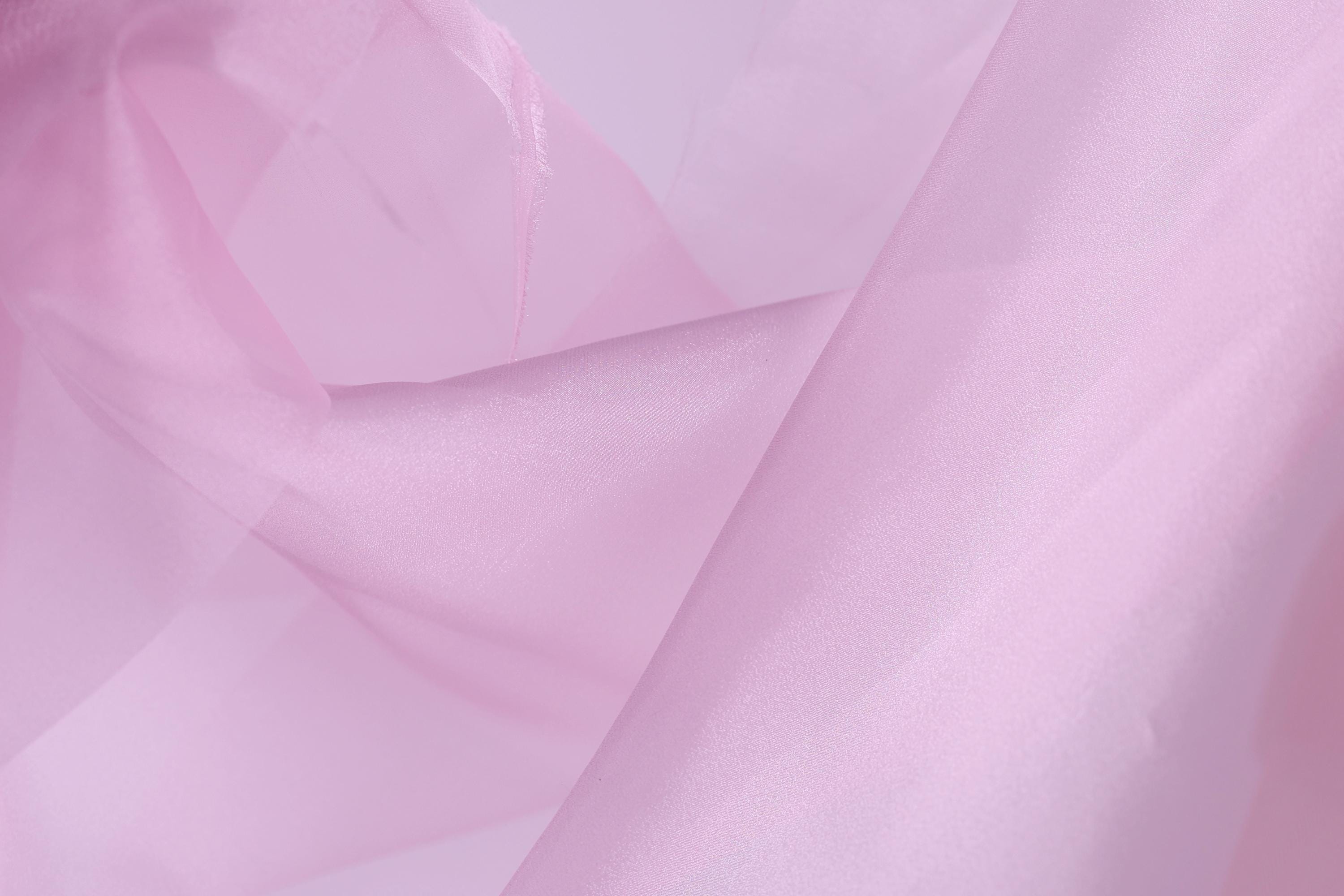 The image is a close-up of a soft, light pink fabric, possibly silk or chiffon, with a slightly wrinkled texture.