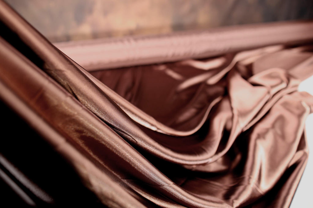 a close-up view of a piece of shiny, brown fabric, possibly silk or satin, with a blurred background.