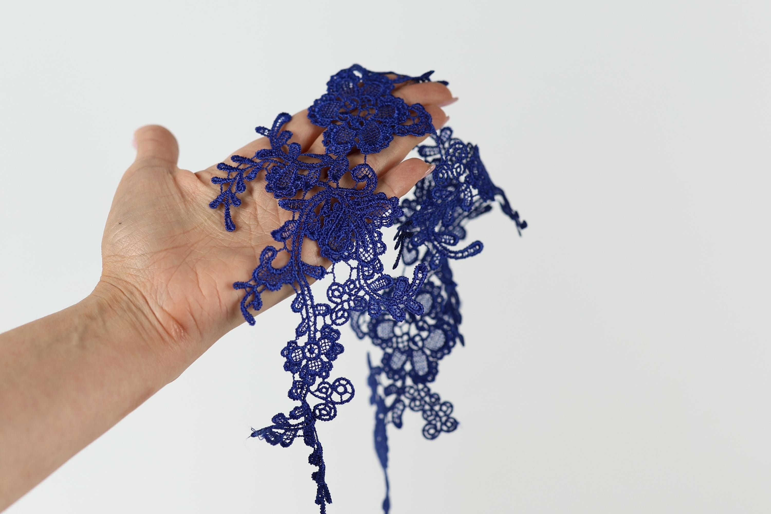 A hand holding a piece of blue lace against a white background.