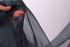 A hand holding a piece of dark grey fabric, with the fingers visible and the thumb partially covering the fabric.