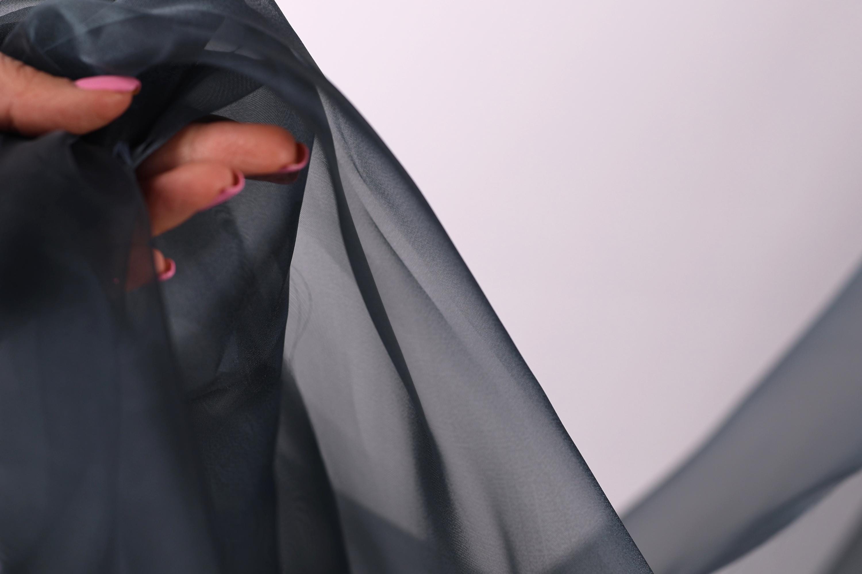 A hand holding a piece of dark grey fabric, with the fingers visible and the thumb partially covering the fabric.