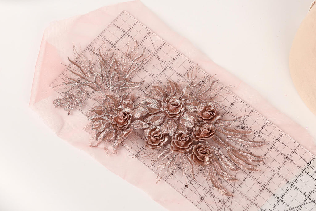 a pink fabric with a floral design, including a group of rose-shaped flowers and leaves. The fabric is laid out on a pink measuring mat, which is placed on a white surface.