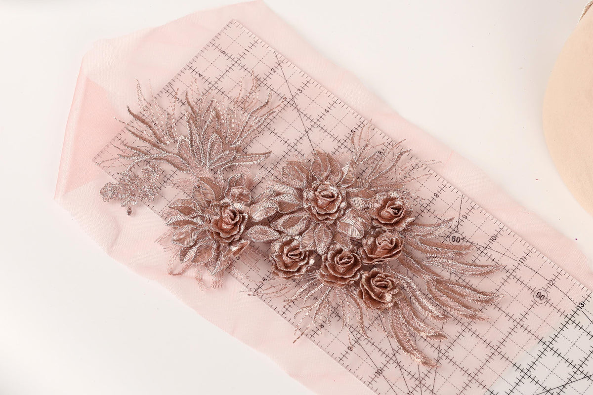 a pink fabric with a floral design, including a group of rose-shaped flowers and leaves. The fabric is laid out on a pink measuring mat, which is placed on a white surface.