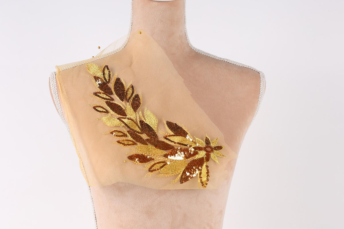 A mannequin with a beige fabric piece featuring a gold and brown floral embroidered design.