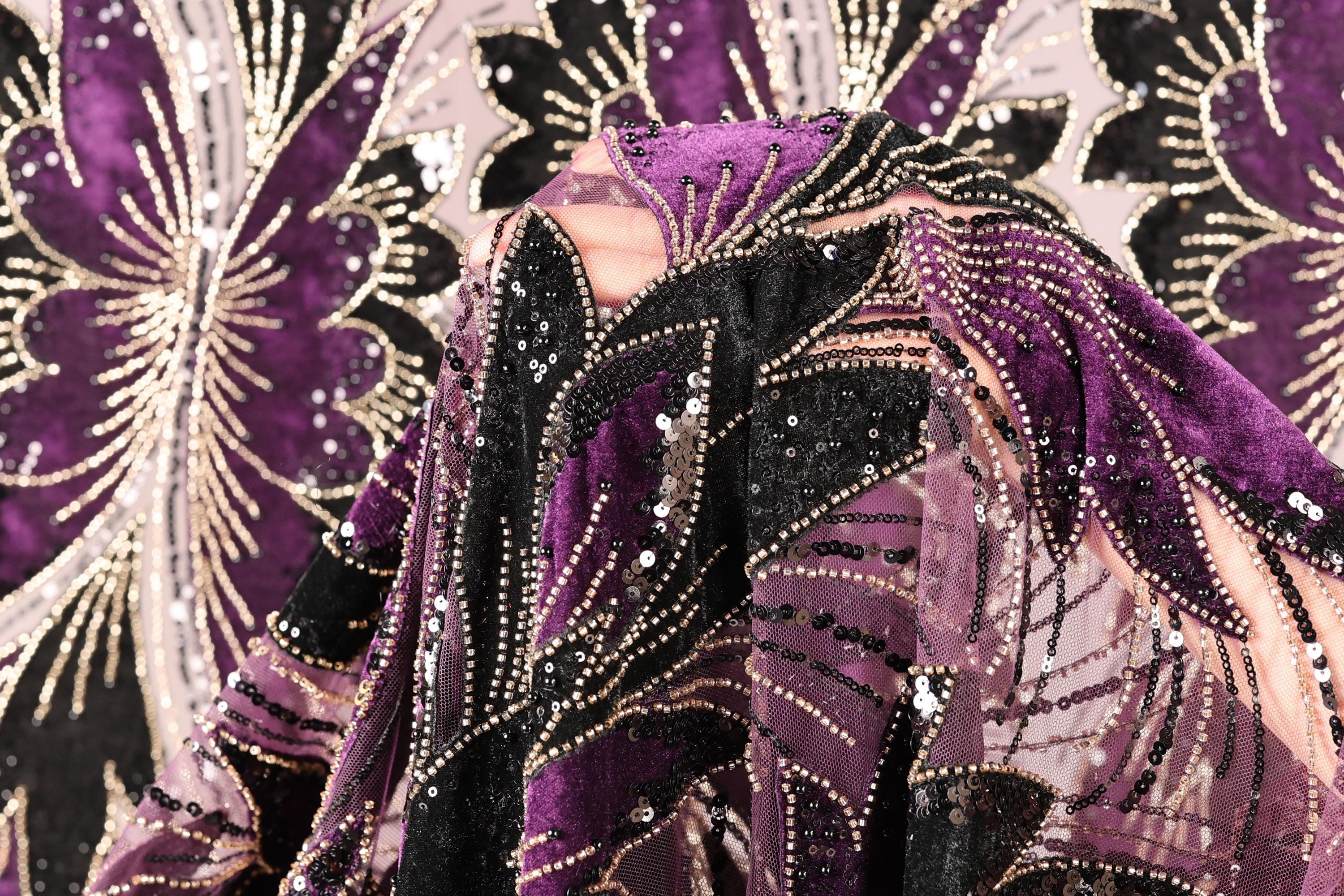 a close-up view of a fabric with a vibrant purple and black pattern, adorned with sequins and beads. The fabric appears to be a piece of clothing or textile, with the intricate design and embellishments making it visually striking.
