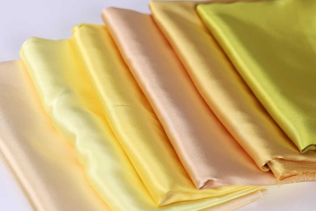 A close-up image of a pile of colorful fabric, including yellow, orange, and green, arranged in a visually appealing manner.