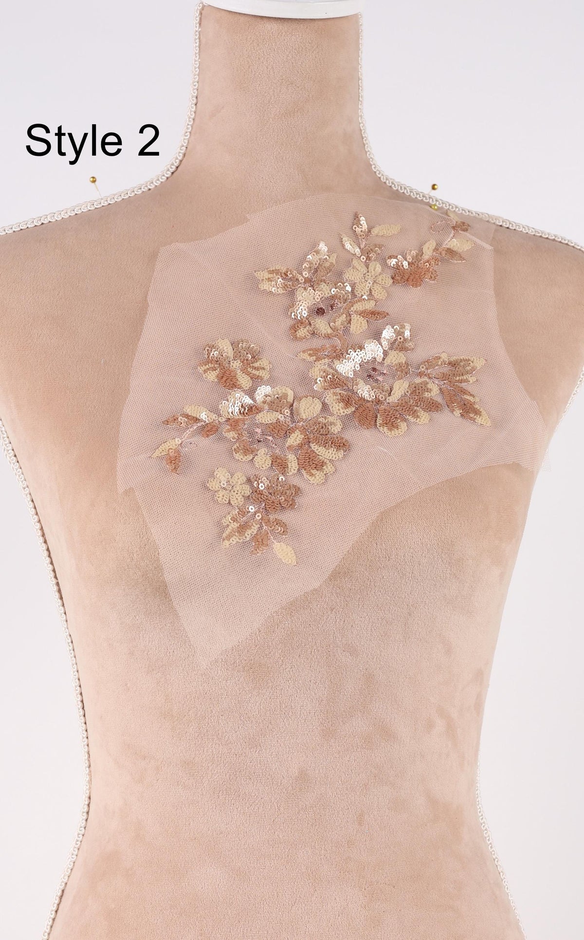 A mannequin with a decorative fabric piece on its shoulder, featuring a floral pattern in gold and white colors.