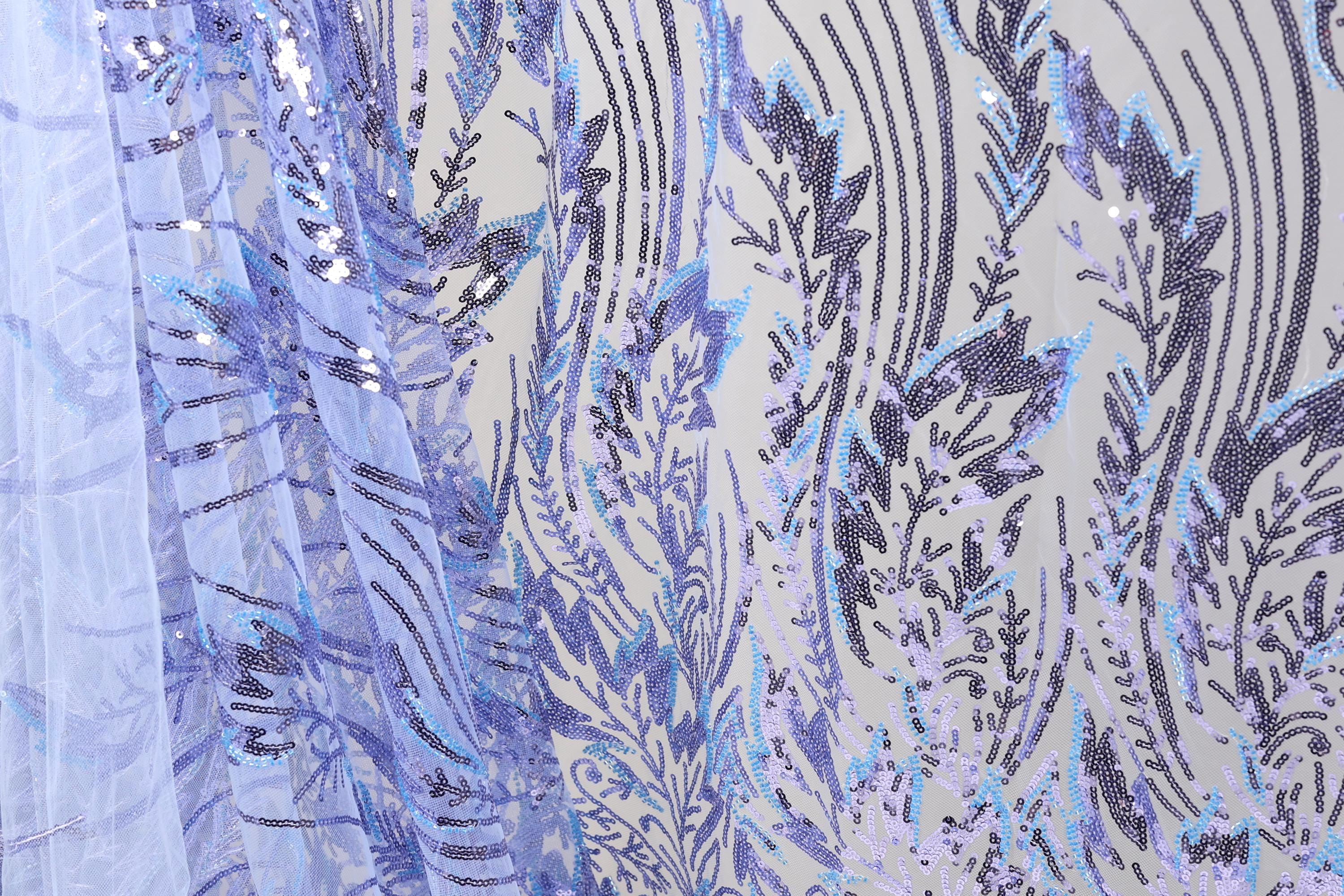 a close-up view of a fabric with a floral pattern and sequin details. The fabric appears to be a sheer material, with a blue and purple color scheme. The pattern consists of various floral motifs and sequin elements, creating a visually striking and intricate design.