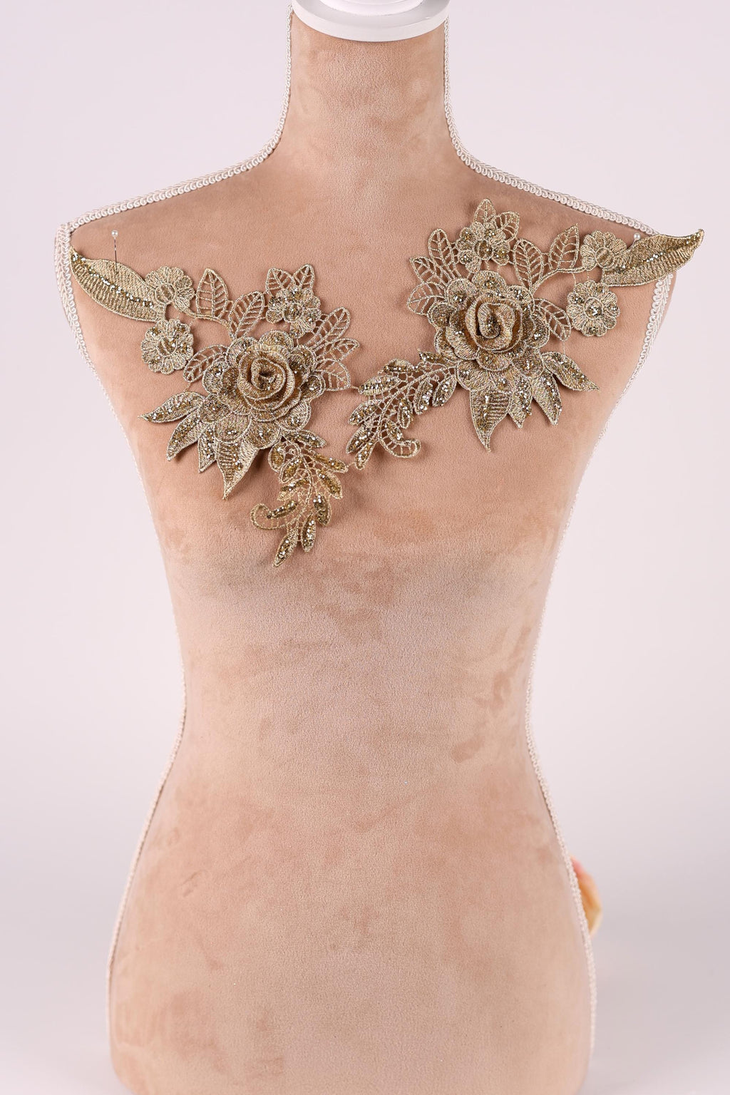 A mannequin with a beige body and gold floral embellishments on the shoulders.