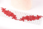 a piece of red lace with intricate floral patterns laid out on a transparent ruler, which is placed on a white surface.