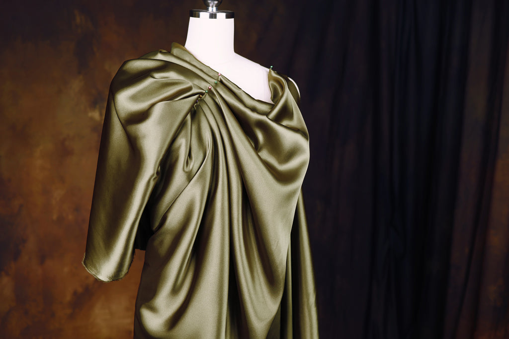 A mannequin wearing a green satin dress with a draped, flowing design.