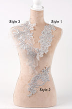 A mannequin wearing a white dress with various lace and floral patterns on its neckline and sides.