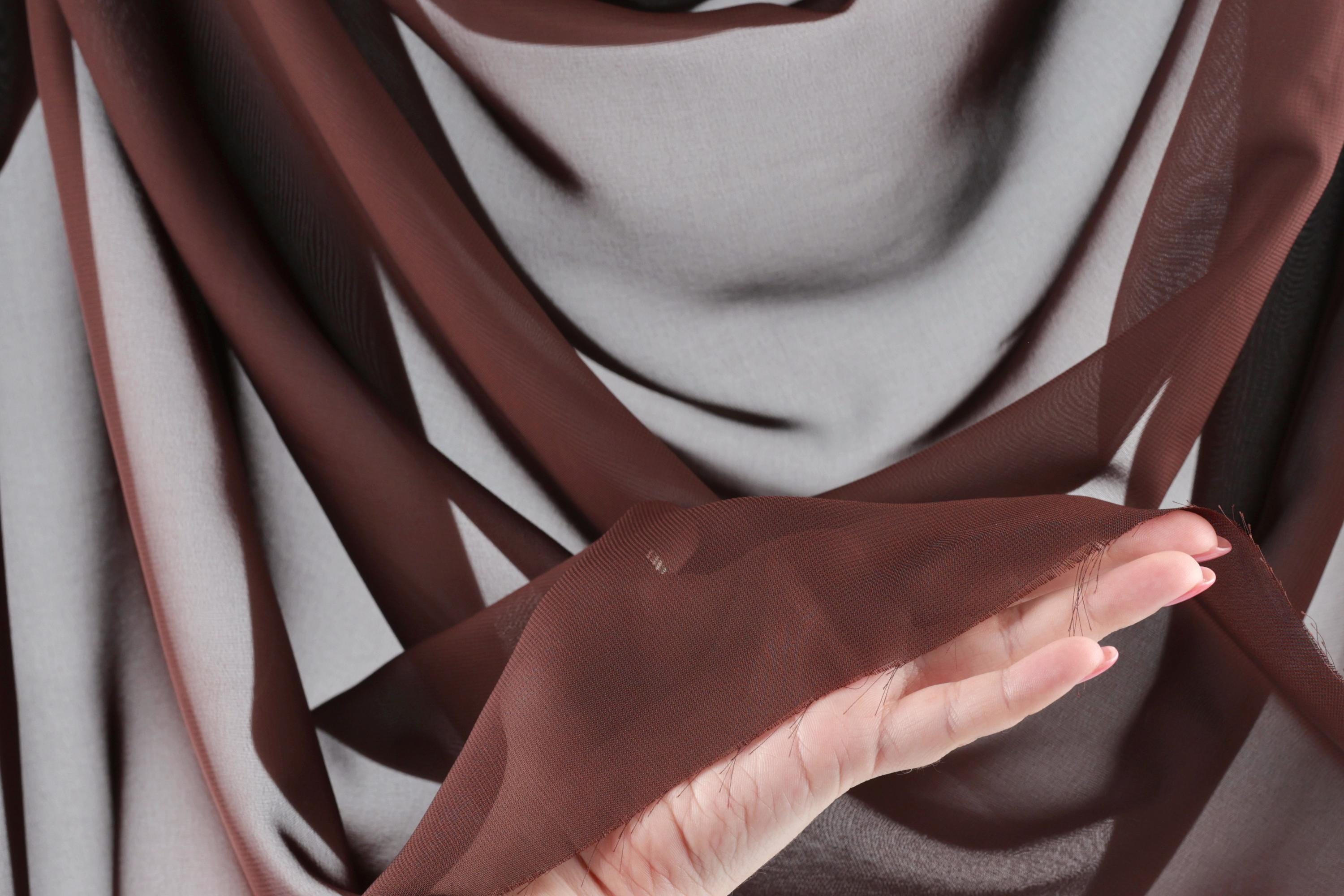 A close-up view of a hand holding a piece of brown fabric, with the fabric appearing to be made of sheer material.