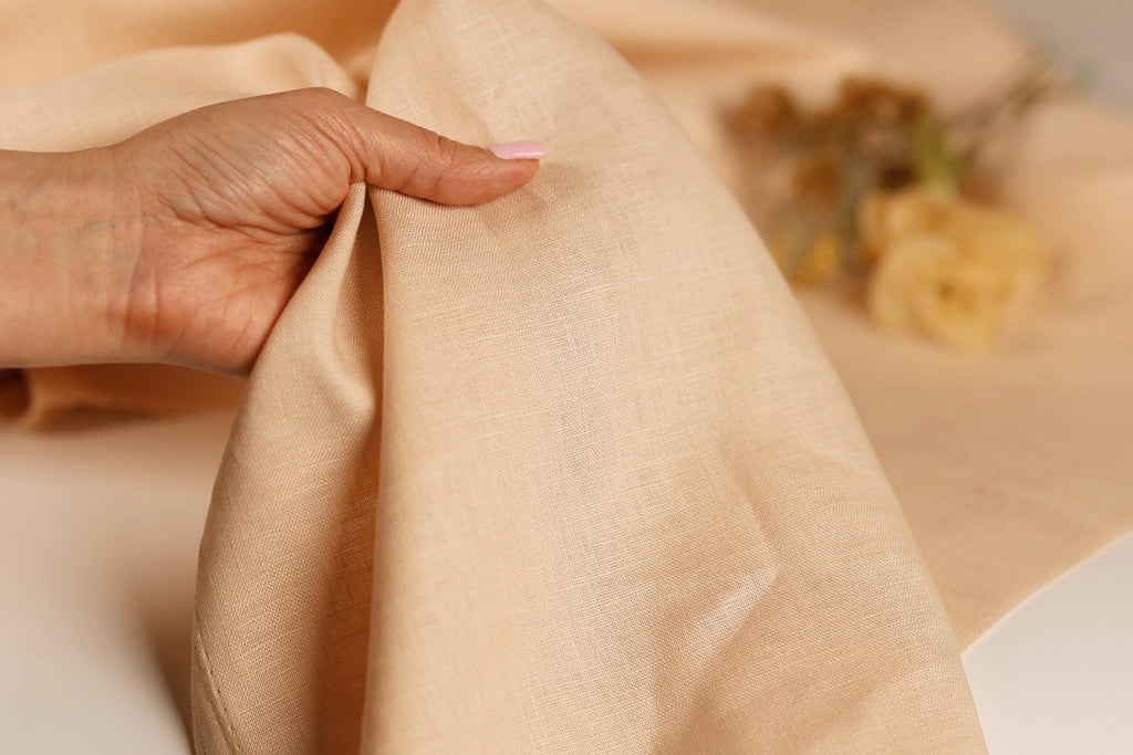 A hand is holding a piece of light-colored fabric, possibly linen, in the foreground of the image.
