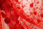 The image is a close-up of a red fabric with a floral pattern, featuring red roses and other flowers.
