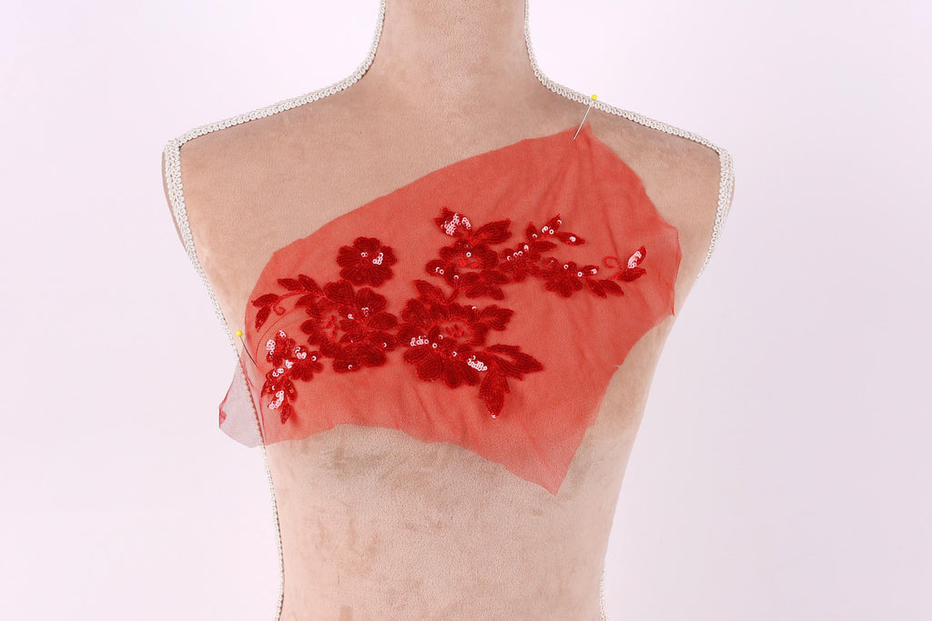 A mannequin with a red fabric piece on its chest, featuring a floral pattern and sequins.