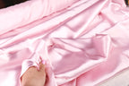 A hand is holding a piece of pink satin fabric, which appears to be a soft and smooth material.