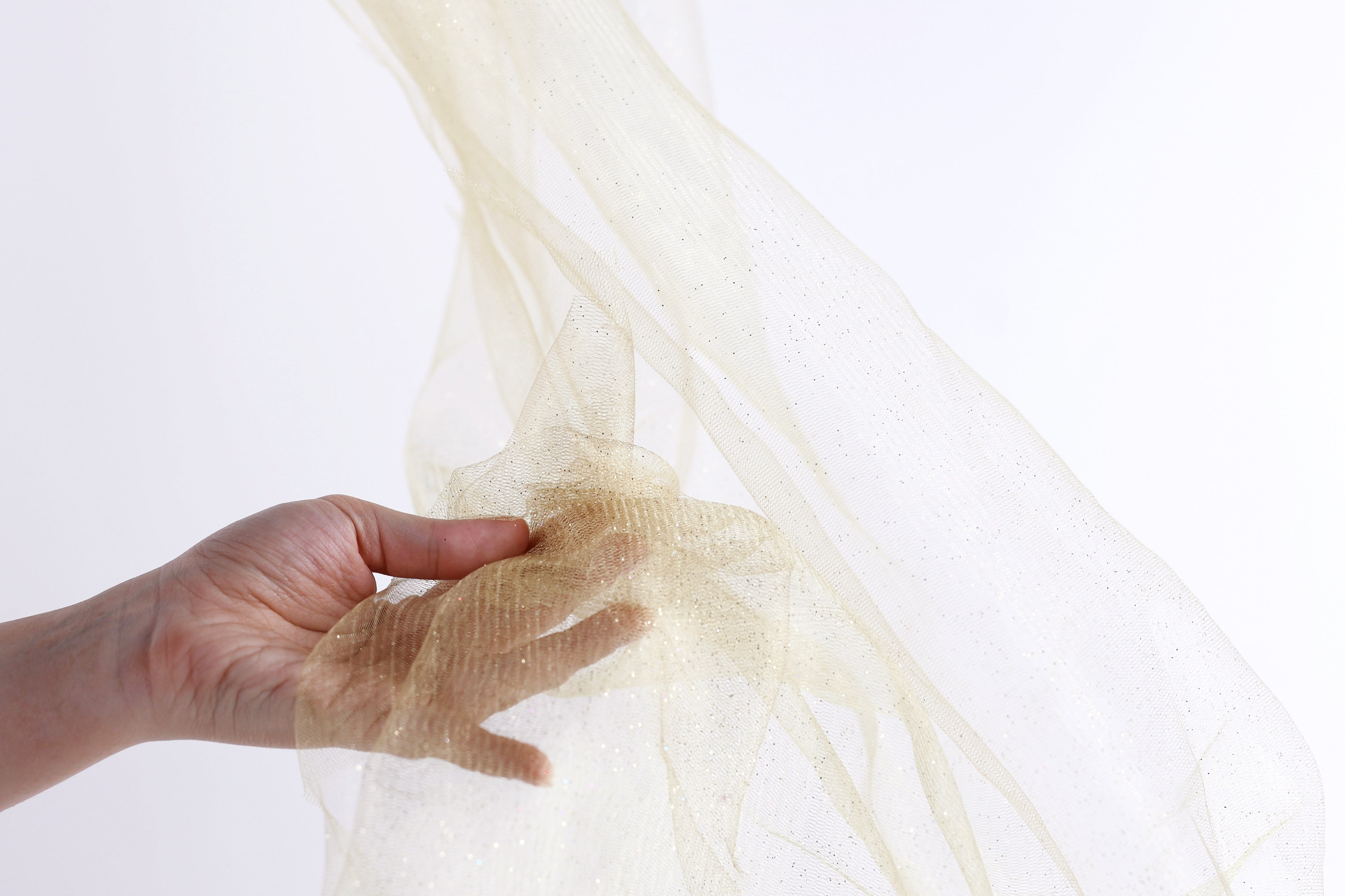 A hand is holding a piece of gold glittery fabric against a white background.