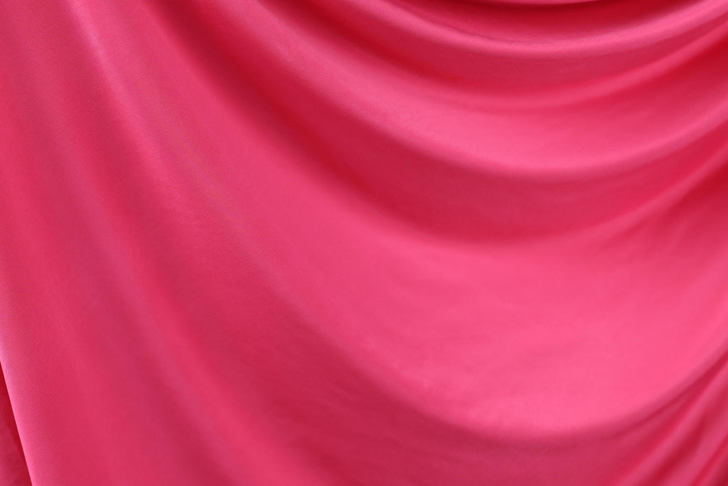 The image is a close-up of a bright pink fabric, possibly silk or chiffon, with a smooth and flowing texture.