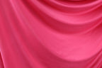The image is a close-up of a bright pink fabric, possibly silk or chiffon, with a smooth and flowing texture.