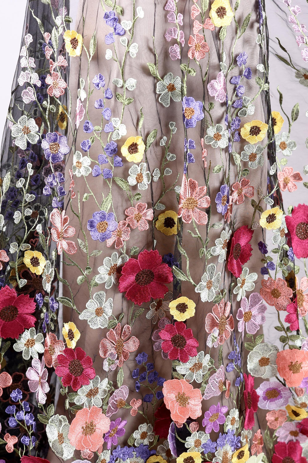 a close-up view of a fabric with a vibrant floral pattern. The fabric is adorned with a variety of colorful flowers, including red, pink, yellow, and purple flowers, creating a visually striking and intricate design. The flowers are arranged in a way that they appear to be growing upwards, adding a sense of depth and dimension to the fabric. The image does not contain any text or other discernible objects, and the focus is solely on the detailed floral pattern on the fabric.