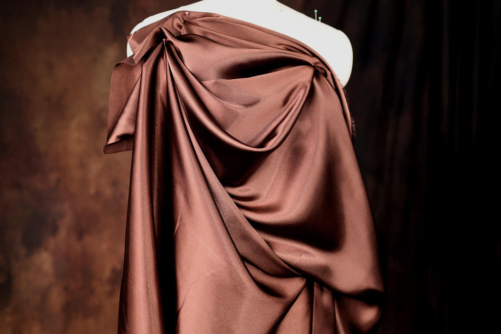 A mannequin wearing a brown satin dress with a draped, flowing silhouette.