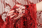 A close-up view of a hand holding a red fabric with intricate black and red sequin designs.