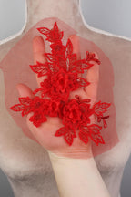 A hand holding a red floral piece against a gray background.
