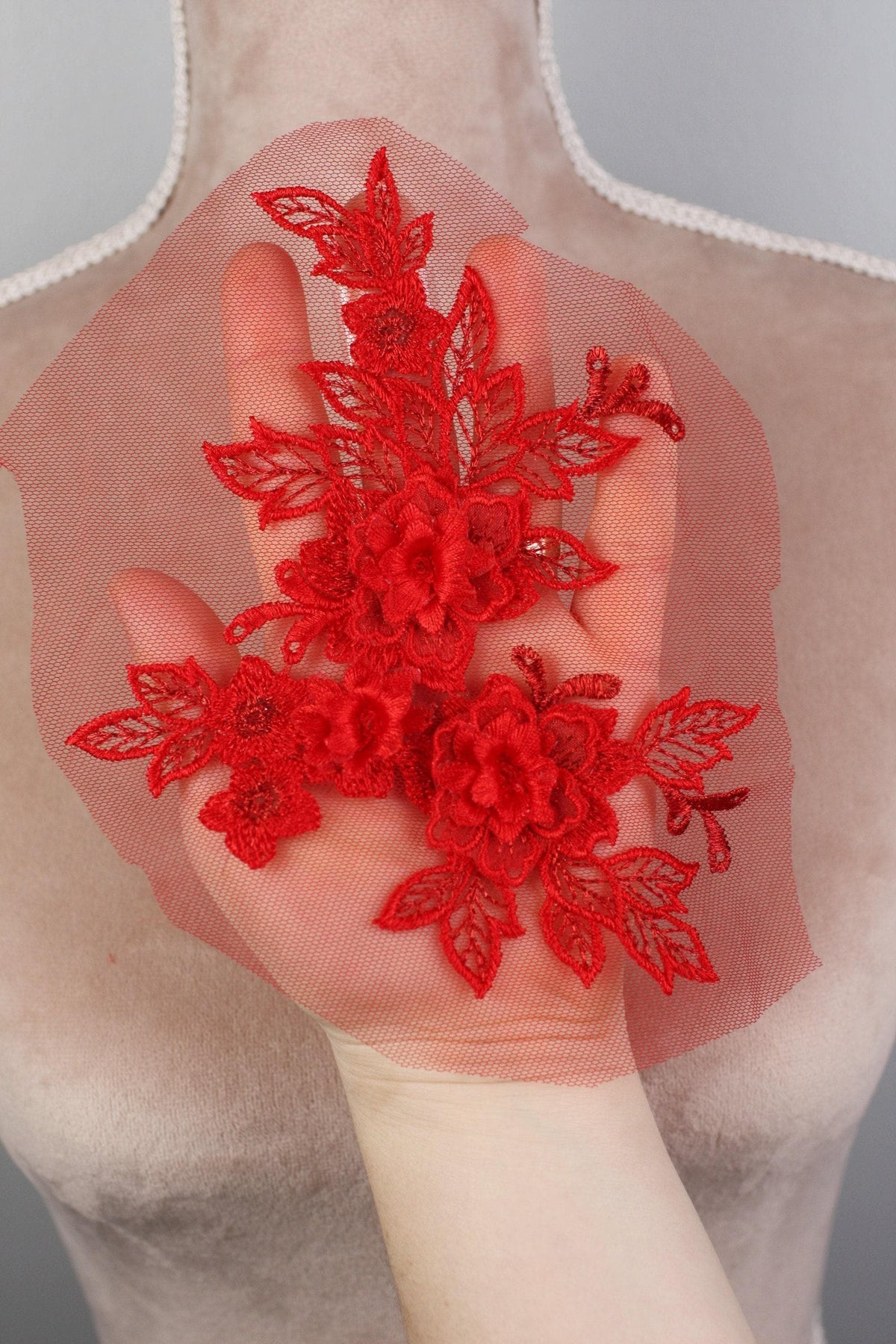 A hand holding a red floral piece against a gray background.