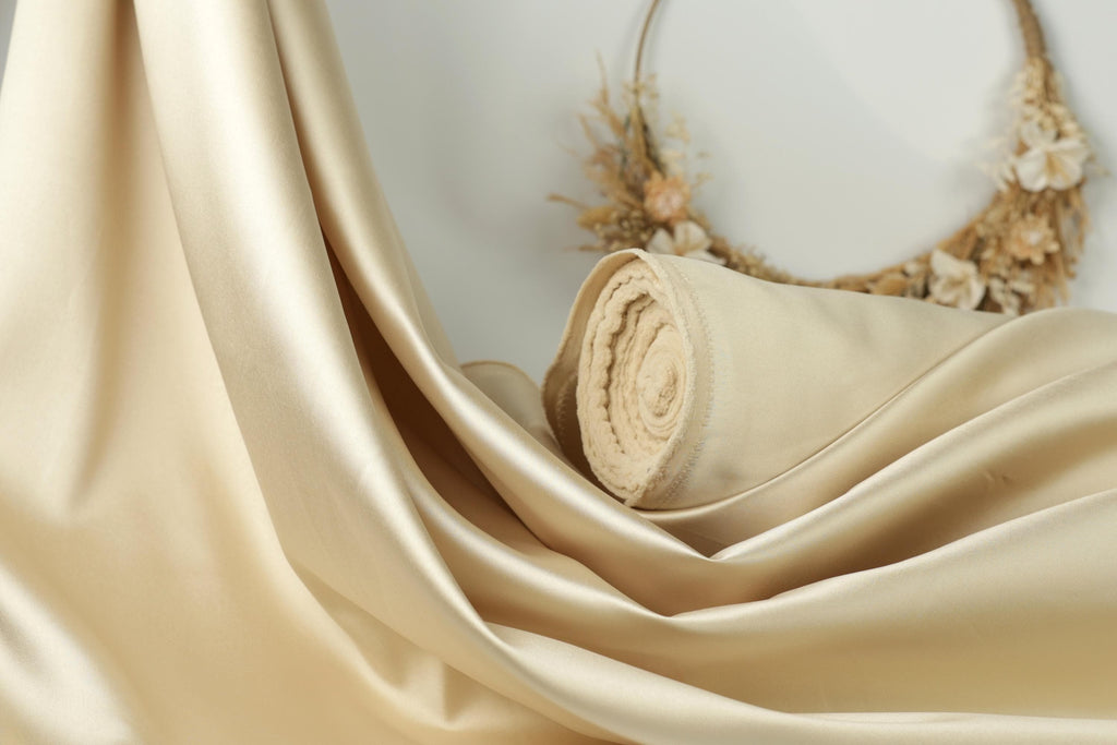 a close-up view of a luxurious, flowing gold satin fabric, with a wreath of dried flowers in the background.