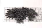 a close-up view of a black lace or fabric with intricate floral or leaf-like patterns. The lace appears to be made of a shiny material, possibly beads or sequins, and is displayed on a ruler for scale.