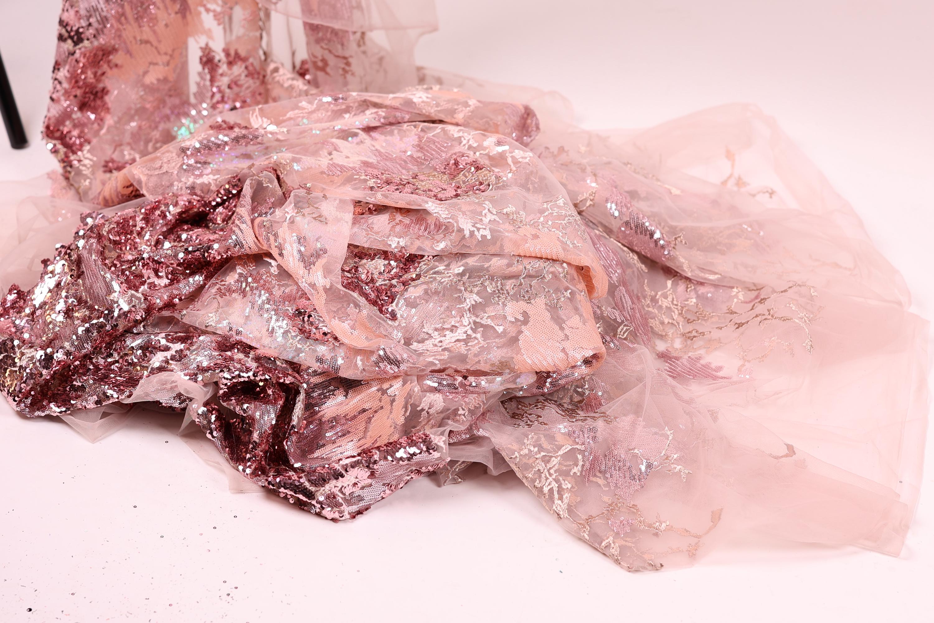 a pile of pink and white fabric with sequins and lace-like patterns, creating a visually appealing and intricate design.