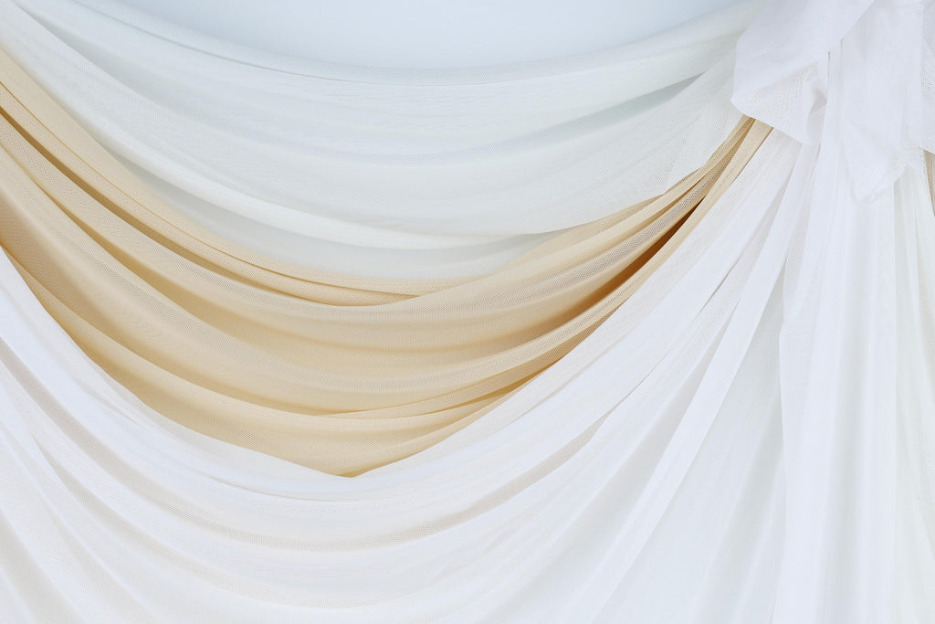 a close-up view of a white and beige fabric, possibly a curtain or drape, with a soft, flowing texture.